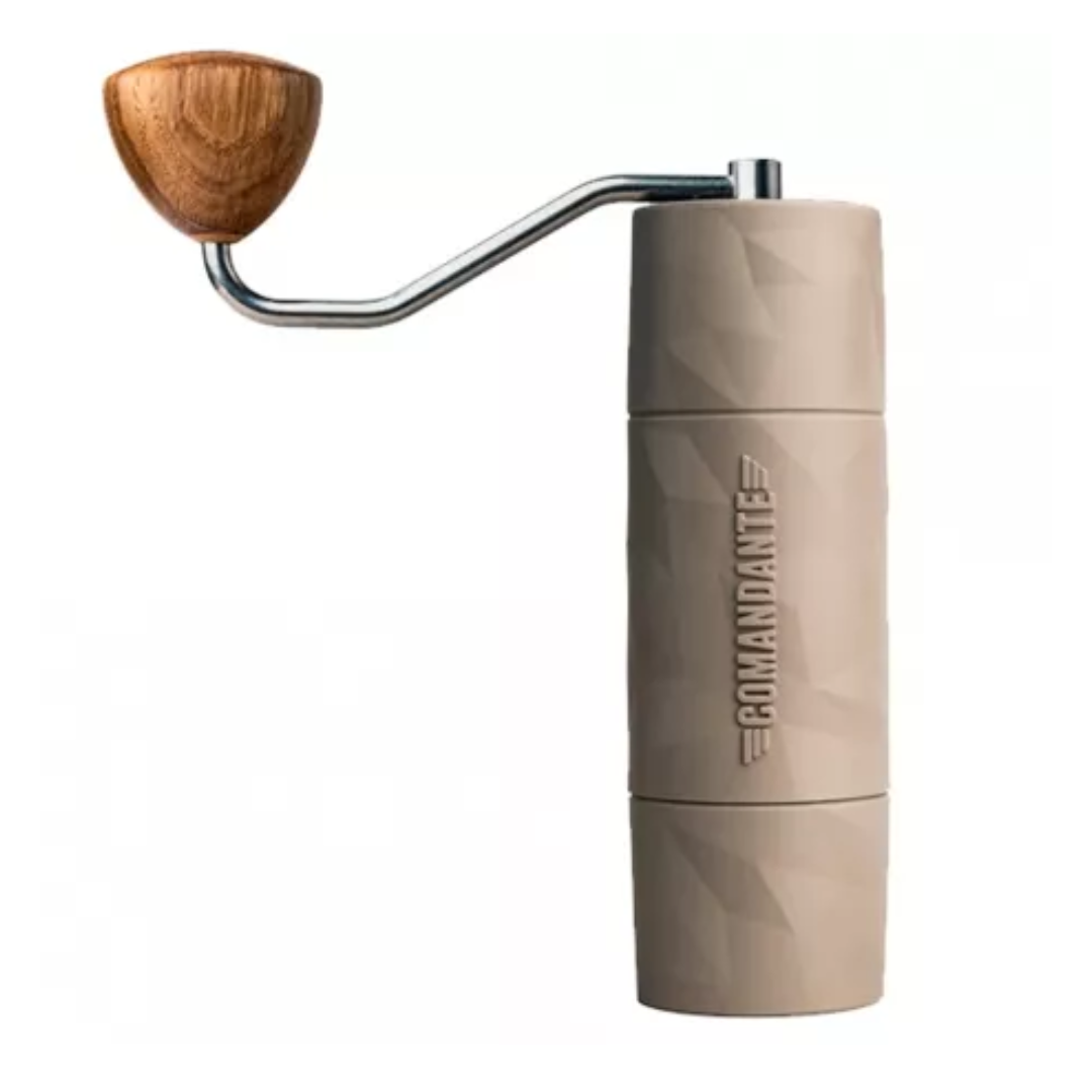 Comandante X25 Trailmaster kaffekværn i farven "Dune". Kværnen har et mat beige udseende med en unik, facetteret overflade, som giver den et robust og moderne look. "Comandante"-logoet er præget i kværnens midtersektion. Den øverste del er udstyret med et ergonomisk håndtag i rustfrit stål, der har en afrundet træknop, hvilket giver et behageligt greb ved brug. Kværnens krop er lavet af avancerede polymere materialer, hvilket gør den ekstremt let og slidstærk, ideel til udendørs brug.