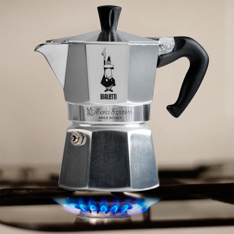 Bialetti Moka Express på et gaskomfur med blå flammer, der varmer espressokanden under bryggeprocessen.