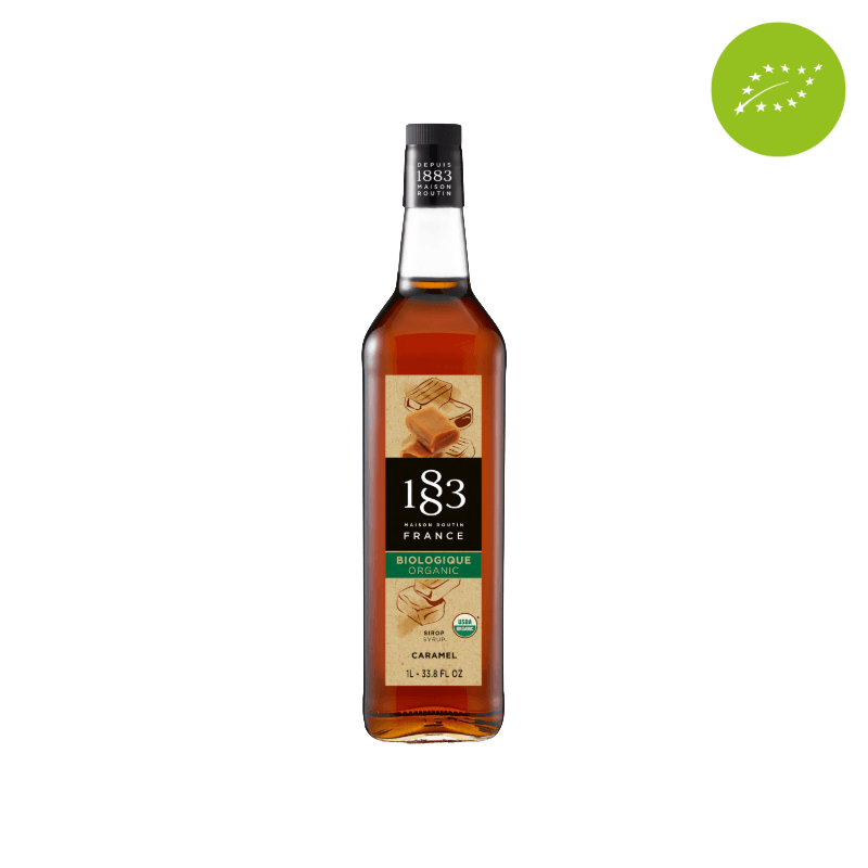 Flaske med 1883 Maison Routin økologiske karamelsirup, 1 liter. Perfekt til at tilføje en sød og fyldig karamelaroma til kaffe, desserter og andre drikkevarer. I højre hjørne ses et øko mærke.