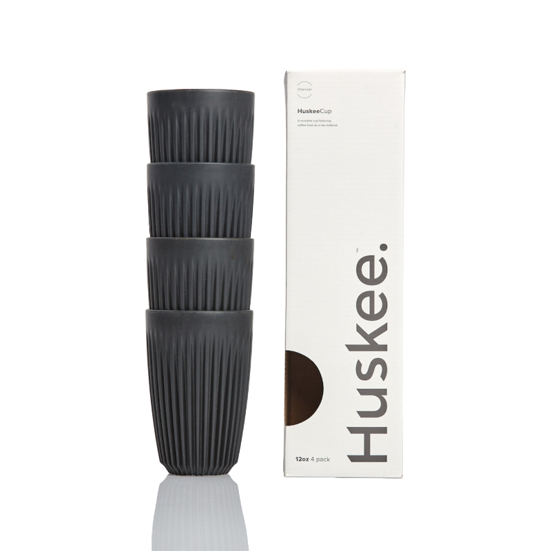 Fire kulfarvede Huskee-kopper i størrelsen 12 oz er arrangeret stakket ved siden af deres originale emballage, der fremhæver materialets genanvendelighed.