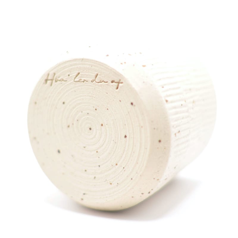 Detaljeret visning af bunden af en beige keramikkop med smalle riller med indgraveret logo.