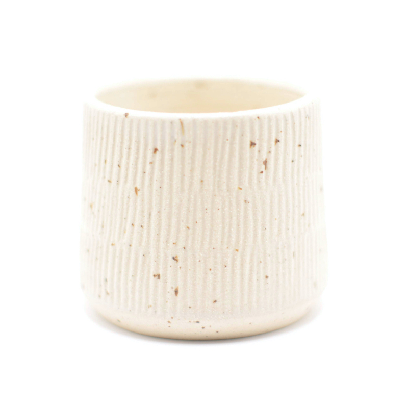 En minimalistisk beige keramikkop med vertikale riller, skabt i keramik.