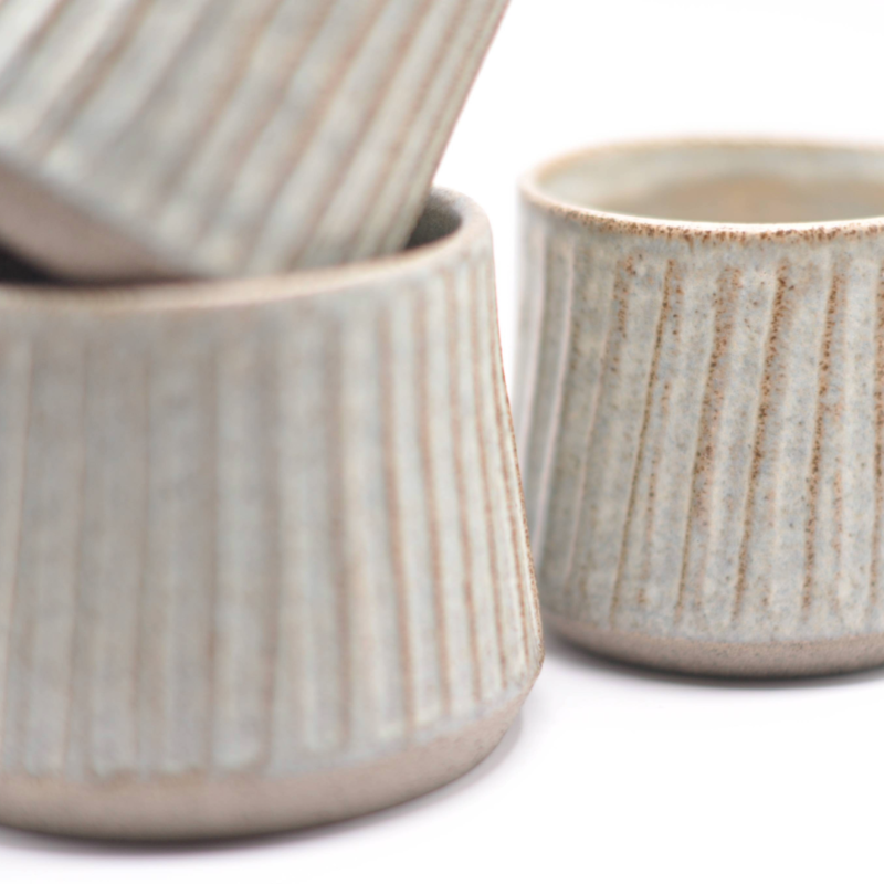 En blå keramikkop med brede riller fotograferet fra en lav vinkel for at fremhæve den strukturerede overflade.