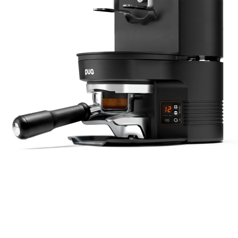 Nærbillede af PUQpress M3 tamper i aktion, hvor et portafilter er placeret under enheden for præcis tampning.