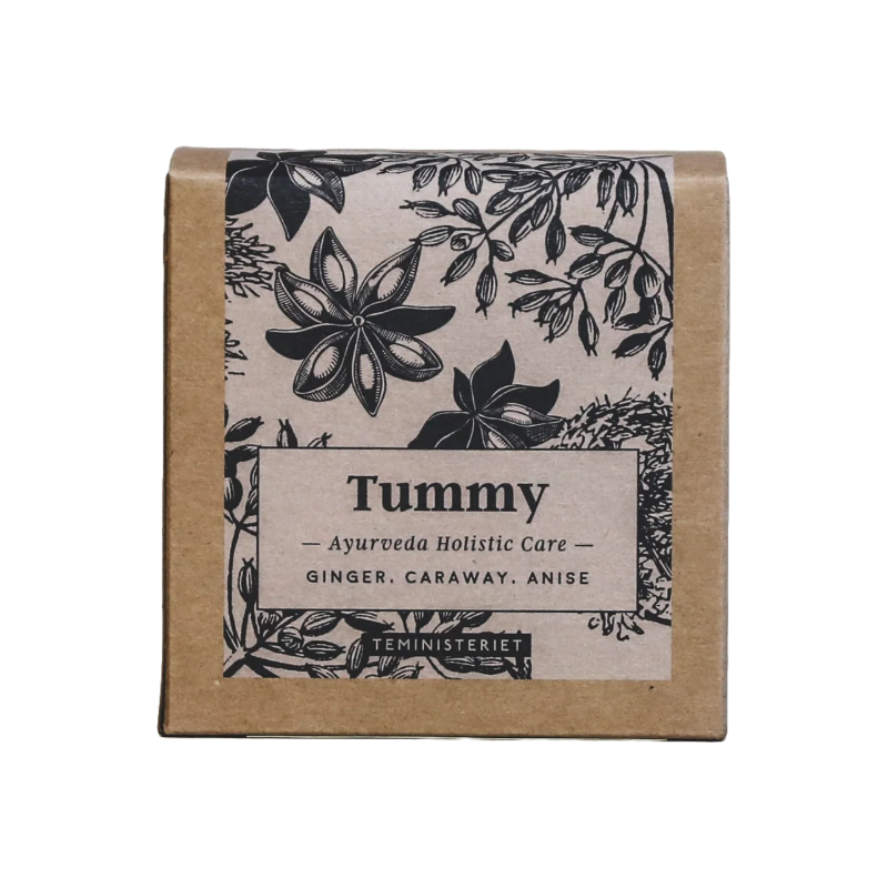 Teministeriet Ayurveda Tummy te i en kvadratisk, brun papæske med et botanisk design. Forsiden har en sort-hvid illustration af krydderurter og krydderier, herunder anis, kommen og ingefær, der omkranser en etiket med produktnavnet "Tummy" i fed skrift. Under dette står "Ayurveda Holistic Care" efterfulgt af ingredienserne: ingefær, kommen og anis. Nederst ses mærket "Teministeriet". Designet har en naturlig, håndtegnet æstetik, der understøtter det ayurvediske og holistiske tema.