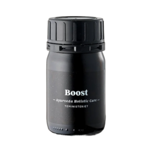 Glas med Ayurveda Boost Te. Sort tebeholder med teksten "Boost – Ayurveda Holistic Care" fra Teministeriet. Beholderen er cylindrisk med en sort skruelåg og minimalistisk design.