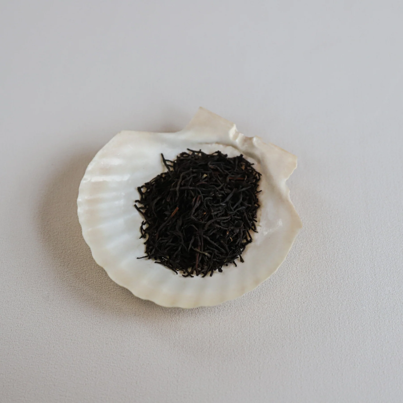 Løsbladste placeret på en muslingeskal. Teen består af sorte, snoede teblade, som ser tørrede og aromatiske ud, typisk for Earl Grey-te.