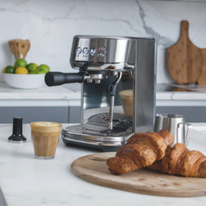 Sage Bambino Plus espressomaskine på et moderne køkkenbord med serveret kaffe og friskbagte croissanter.