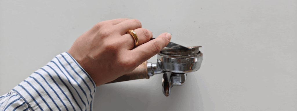 En hånd skiller filterkurven fra portafilteret ved hjælp af en filterkurvaftager