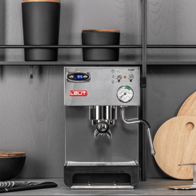 Lelit Anna espressomaskine i køkkenmiljø med sort tilbehør i baggrunden.
