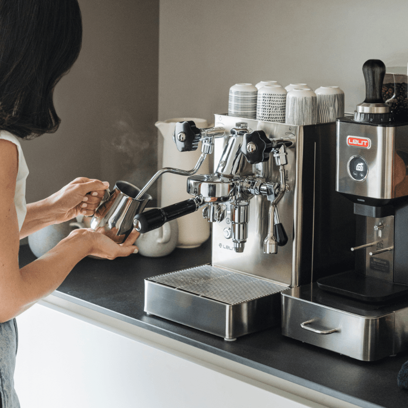 Person steamer mælk på Lelit MaraX i rustfrit stål på køkkenbord.