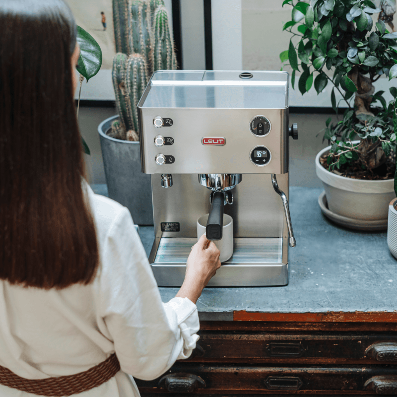 Kvinde brygger espresso på Lelit Elizabeth espressomaskine i et køkken med grønne planter.