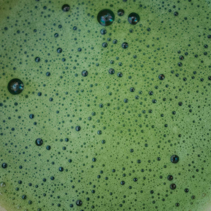 æt makrofoto af intens grøn matcha-skum med tusindvis af små bobler og glinsende overflade; detaljeret visning af skummets tekstur og farvemætning.