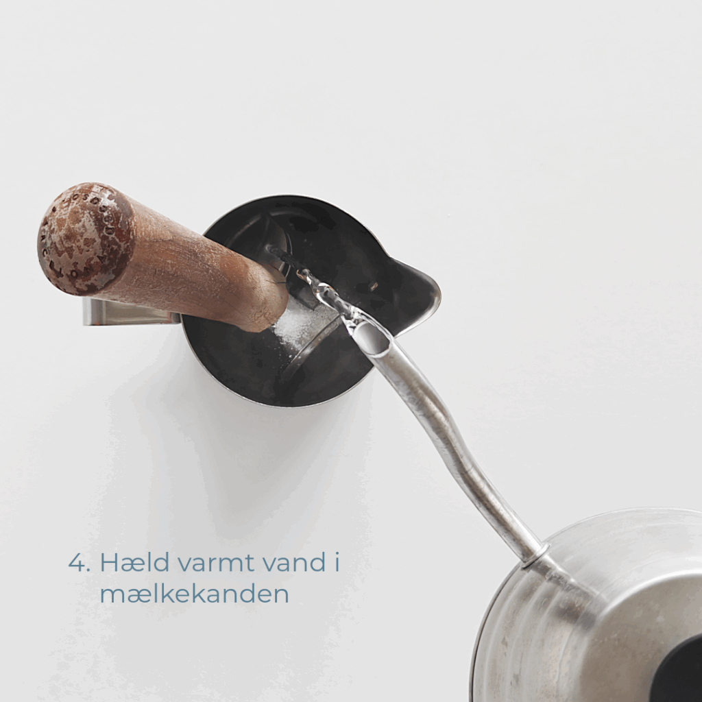 Varmt vand hældes i mælkekanden med portafilter og espressorens.