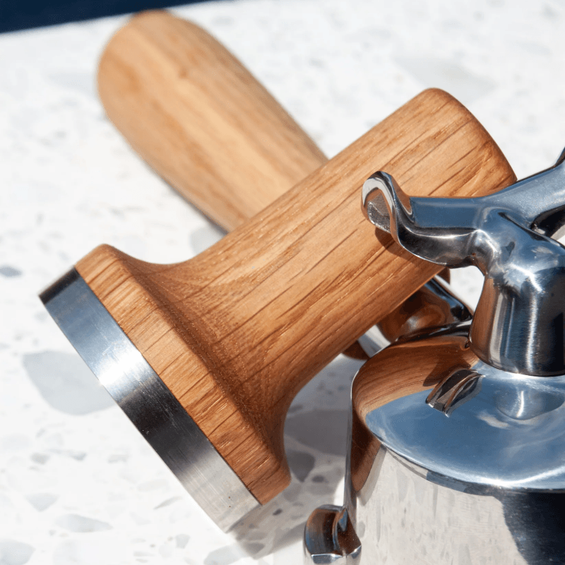 Baark The Sage Tamper i eg – placeret ved siden af et portafilter på en bordplade.