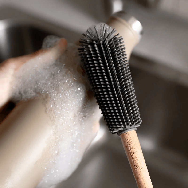 Stemningsbillede af AYA&IDA flaskebørste i brug: silikonehovedet skrubber en flaske med sæbeskum, fokus på børstens rengøringseffekt.