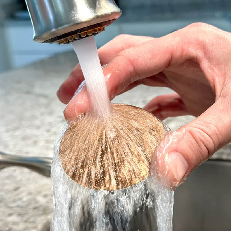 AeroPress Gold Tone Metalfilter — hånd holder det kobberfarvede metalfilter under rindende vand for at skylle det, praktisk rengøringseksempel.