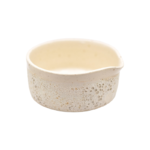 Håndlavet matcha-skål fra "Hva' ler du af" set skråt forfra; rå, beige stentøj med porøs struktur i nederdelen, glat inderside og lille hældetud — unikt, rustikt finish.