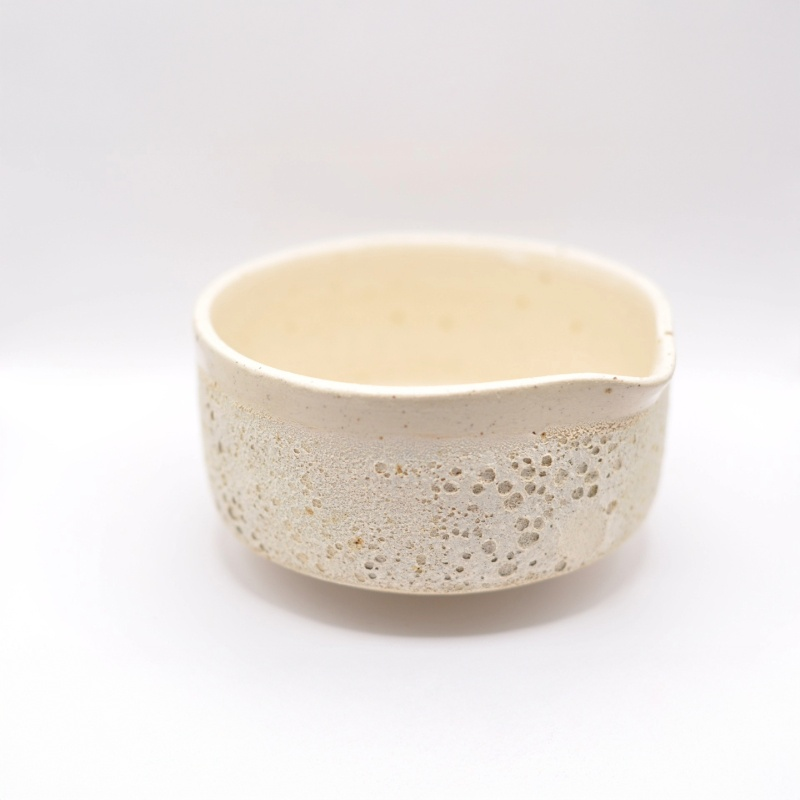 Matcha-skål i beige, hånddrejet stentøj set i lavt perspektiv; porøs tekstur langs skålsiden, let buet hældetud og blød, håndlavet kant.