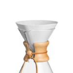 Tæt billede af en Chemex kaffebrygger med et foldet hvidt papirfilter FC-100 placeret i glasskålen og trækrave omkring halsen.