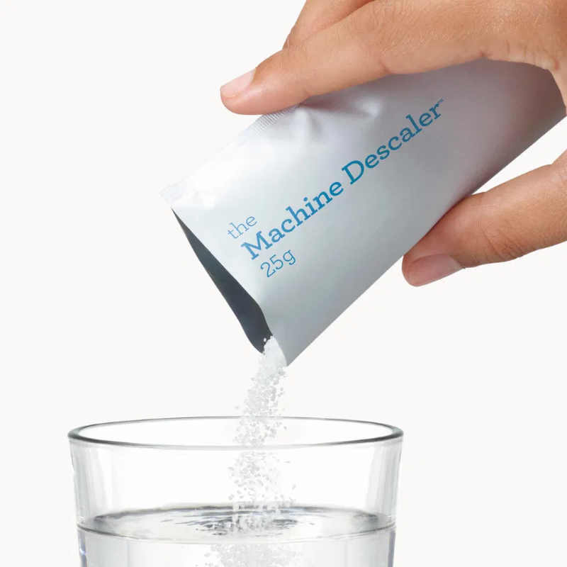 Dosering af afkalker – Hånd hælder hvidt afkalker-pulver fra en 25 g-pose ned i et glas med vand.