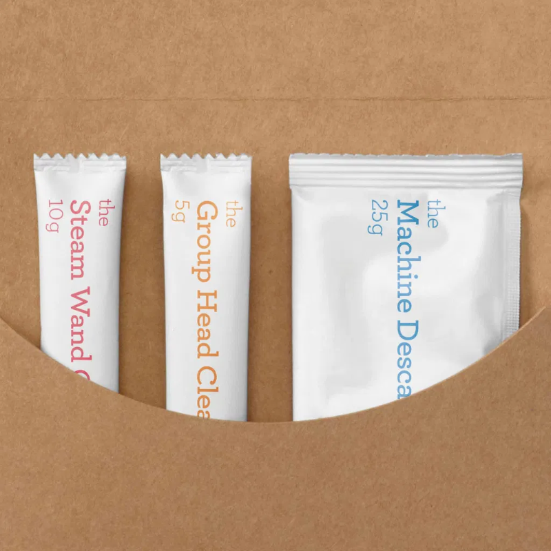 Rensesæt i æske – Nærbillede af tre småposer med rengøringsprodukter i en brun papæske: Steam Wand Cleaner, Group Head Cleaner og Machine Descaler.